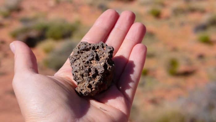 A close-up of a hand holding a rough volcanic stone in a desert landscape.